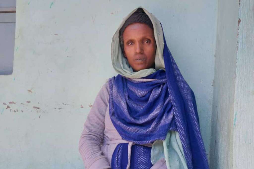 donna etiope vestito blu, seduta su una panchina davanti a edificio con muro azzurro chiaro